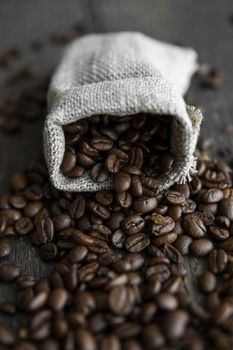 Coffee beans scattered from a linen bag on a wooden table. Fresh roasted arabica coffee beans