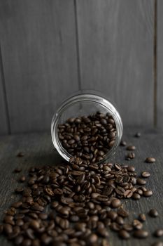 Roasted fresh arabica coffee beans scattered on a table from a little jar on a wooden table. Fresh coffee beans