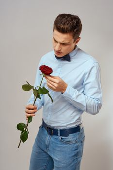 Romantic man with a red rose and in a blue shirt with a bow tie around his neck gray background. High quality photo