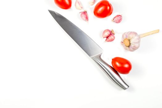 Closeup image of chief knife , garlic and tomato on white table