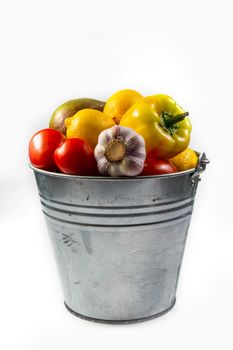 Aluminum bucket with assortment of fresh vegetables on white background.