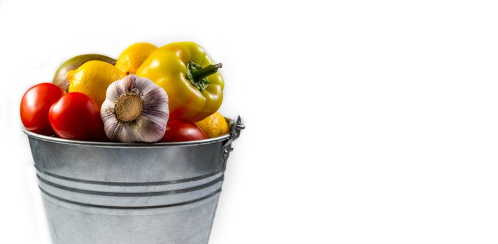 Aluminum bucket with assortment of fresh vegetables on white background.