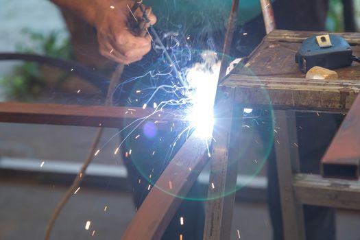 Close-up of hands A man holding a welding machine and doing spot welding under the canopy of his garage. Sparks fly away. No protective gloves on hands.