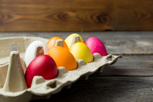 Dyed easter eggs in cardboard box on wooden background. Easter background