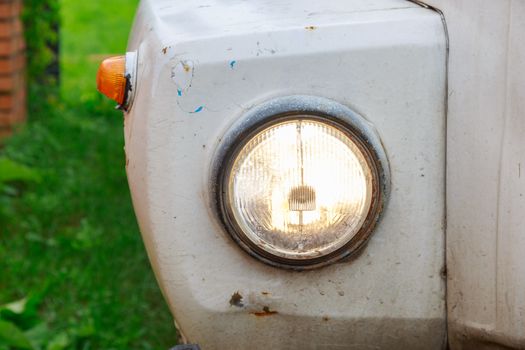 Close up of the headlight of an old abandoned truck with rusted white panels.