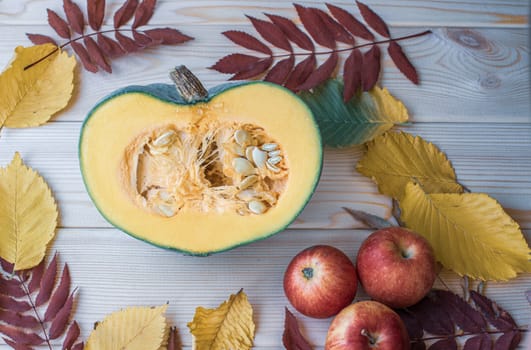 Cut ripe, yellow pumpkin on a wooden background with autumn leaves and red apples. Autumn background