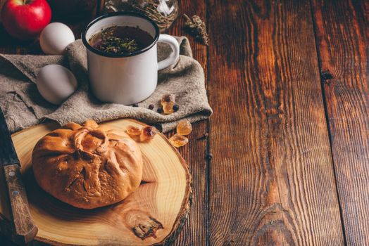 Rustic breakfast with traditional tatar pastry elesh, herbal tea in metal mug, apple and boiled eggs over dark wooden surface