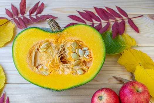 Cut ripe, yellow pumpkin on a wooden background with autumn leaves and red apples. Autumn background