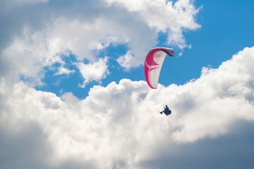 One paraglider is flying in the blue sky against the background of clouds. Paragliding in the sky on a sunny day.