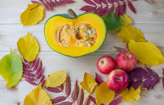 Cut ripe, yellow pumpkin on a wooden background with autumn leaves and red apples. Autumn background