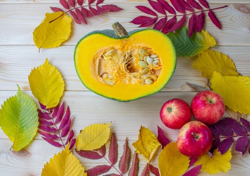 Cut ripe, yellow pumpkin on a wooden background with autumn leaves and red apples. Autumn background