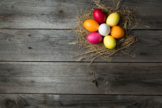 Painted easter eggs in a makeshift straw nest on a wooden background. Easter background, space for text