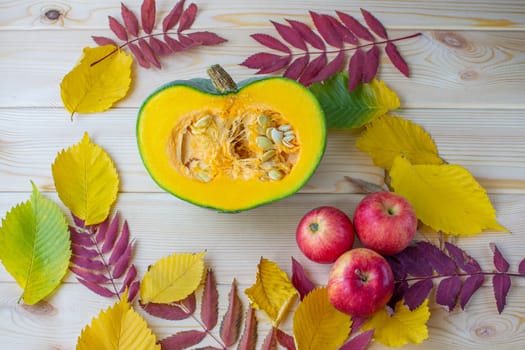 Cut ripe, yellow pumpkin on a wooden background with autumn leaves and red apples. Autumn background