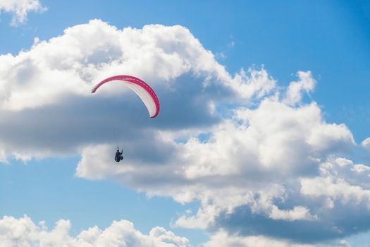 One paraglider is flying in the blue sky against the background of clouds. Paragliding in the sky on a sunny day.