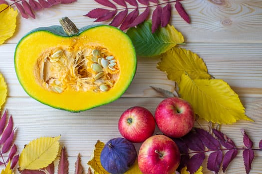 Cut ripe, yellow pumpkin on a wooden background with autumn leaves and red apples. Autumn background