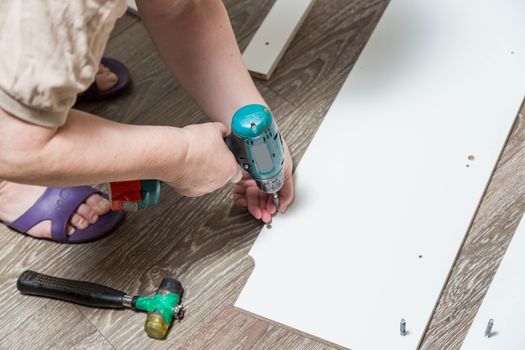 Electric screwdriver with cruciform bat wraps into furniture cabinet, screws lie nearby during assembly of purchased furniture.