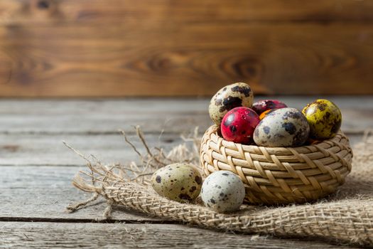 Multi-color dyed Hand painted easter eggs in wicker basket on burlap napkin on wooden background. Easter background with space for a text.Selective focus