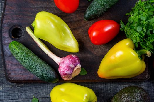 High Angle Still Life View of Wooden Cutting Board Surrounded by Fresh Herbs and Assortment of Raw Vegetables on Rustic Wood Table