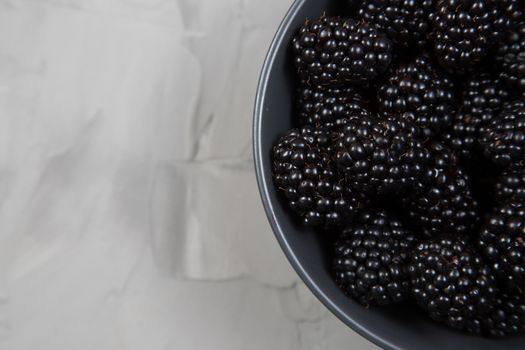 ripe blackberries in a gray ceramic bowl on a concrete background top view