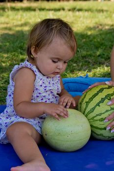 Young woman and little daughter sit in the park on the grass and play with watermelons. Family picnic.