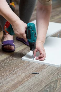 Electric screwdriver with cruciform bat wraps into furniture cabinet, screws lie nearby during assembly of purchased furniture.