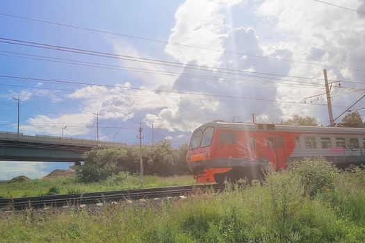 A train with graffiti passes under the bridge over the railway, daytime time, cloudy sky, sunshine, selective focus