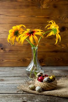 Multi-color dyed Hand painted easter eggs in wicker basket on burlap napkin on wooden background . Still life with flowers. Easter background with space for a text.