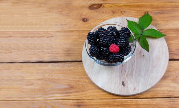 ripe blackberry with leaves on a wooden cutting board in a white ceramic bowl on dark blue wooden background. top view, place for text,