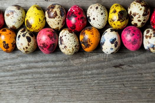 Multi-color dyed easter eggs arranged in a row on wooden background. Easter background with space for a text.