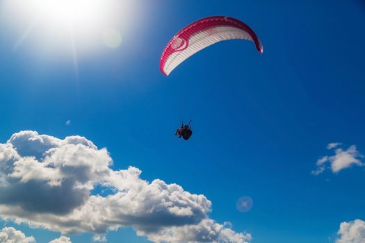 Tandem paraglider is flying in the blue sky against the background of clouds. Paragliding in the sky on a sunny day.