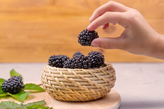 Child's hand takes a blackberry from a wicker bowl on a gray concrete background