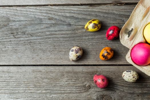 Dyed easter eggs in cardboard box on wooden background. Easter background with space for a text.