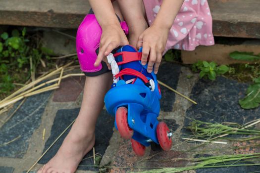 A little girl dresses roller skates sitting on the steps of her country house. The concept of an active healthy lifestyle and safe riding.