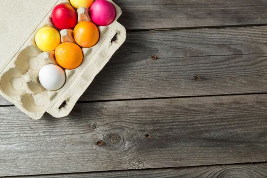 Dyed easter eggs in cardboard box on wooden background. Easter background with space for a text.