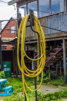 yellow garden hose hanging from a metal pole in the backyard of a country house