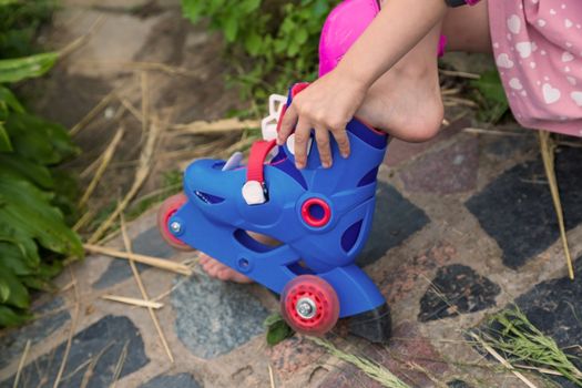 A little girl dresses roller skates sitting on the steps of her country house. The concept of an active healthy lifestyle and safe riding.