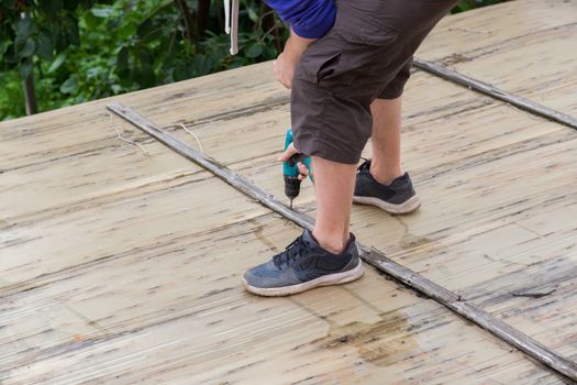 A man holds a screwdriver in his hands while standing on the roof of a village house. Dismantling Old corrugated polycarbonate roof