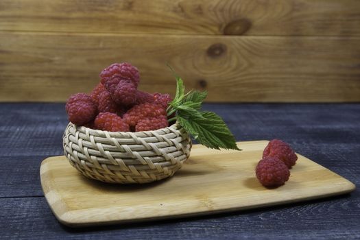 Ripe tasty bright Fresh raspberry in a wicker basket on a cutting board on a wooden background