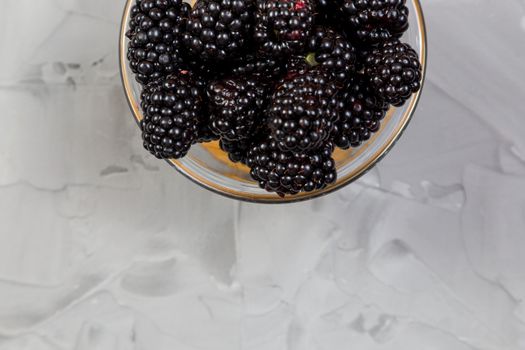 Ripe sweet blackberry in glass bowl on gray concrete background.