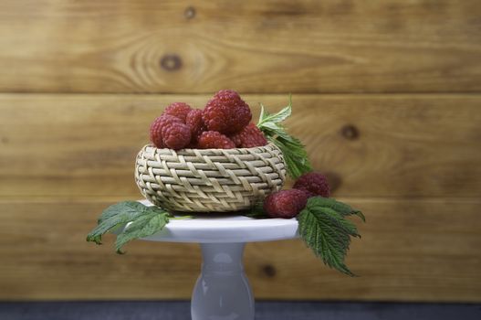 Ripe tasty bright Fresh raspberry in a wicker basket on a cake stand on a wooden background