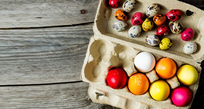 Dyed easter eggs in cardboard box on wooden background. Easter background.