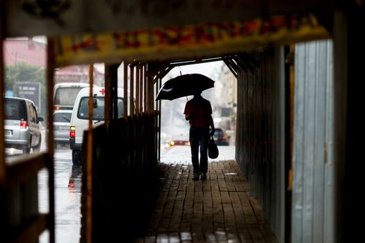 A man walks under an umbrella during the rain, having his face off the camera.