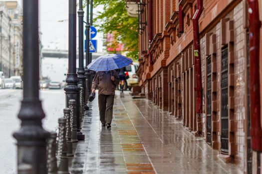 A man walks under an umbrella during the rain, having his face off the camera.