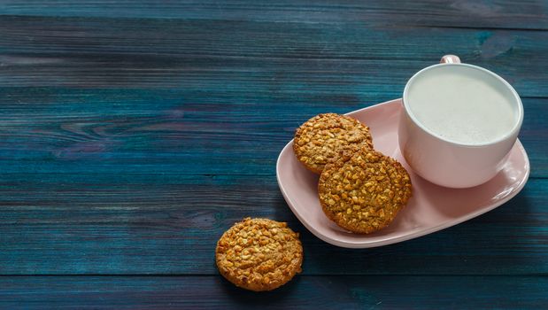 Oatmeal raisin nut cookie and pink cup of coffee with milk on a wooden background in a dark rustic setting