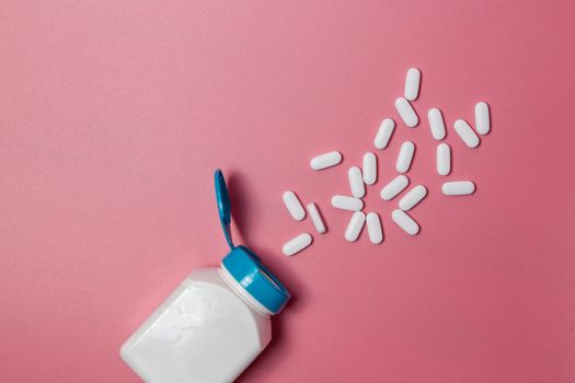 White medical pills and tablets spilling out of a drug bottle. Macro top down view with copy space.