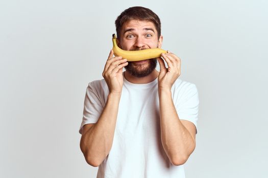 Cheerful man with a banana in his hands on a light background fun emotions Cropped view Copy Space. High quality photo