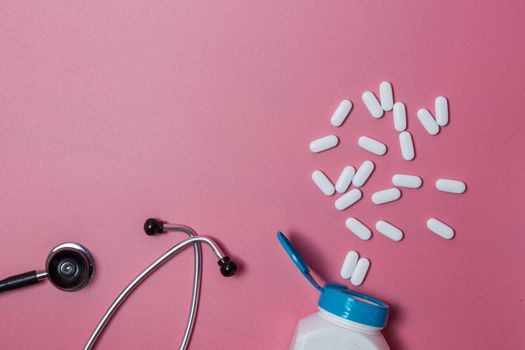 Top view of pills in bottle pack, stethoscope on blue background.