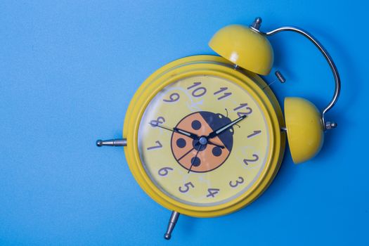 yellow vintage alarm clock on blue background. Time concept.