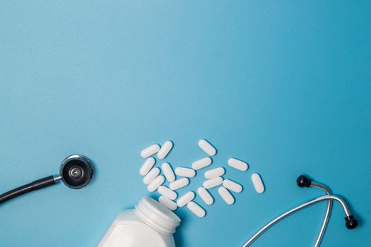Top view of pills in bottle pack, stethoscope on blue background.