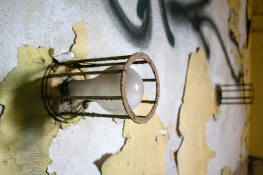 An Old Lightbulb Surrounded by Metal Bars on a Damaged Wall in an Abandoned Building